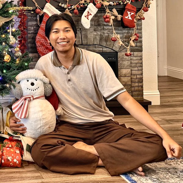 Min sitting by a Christmas tree and fireplace with a snowman plush